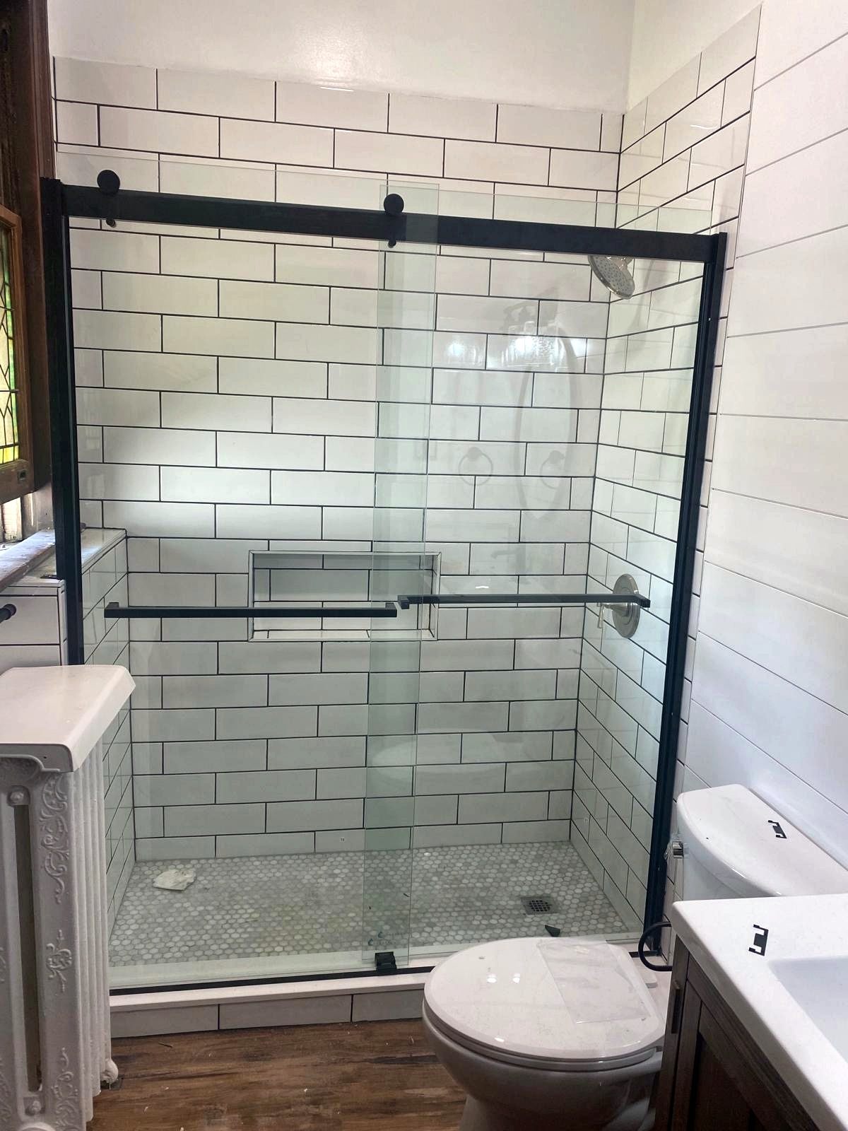 Shower with white subway tile, black grout, hex marble floor, and black sliding glass door