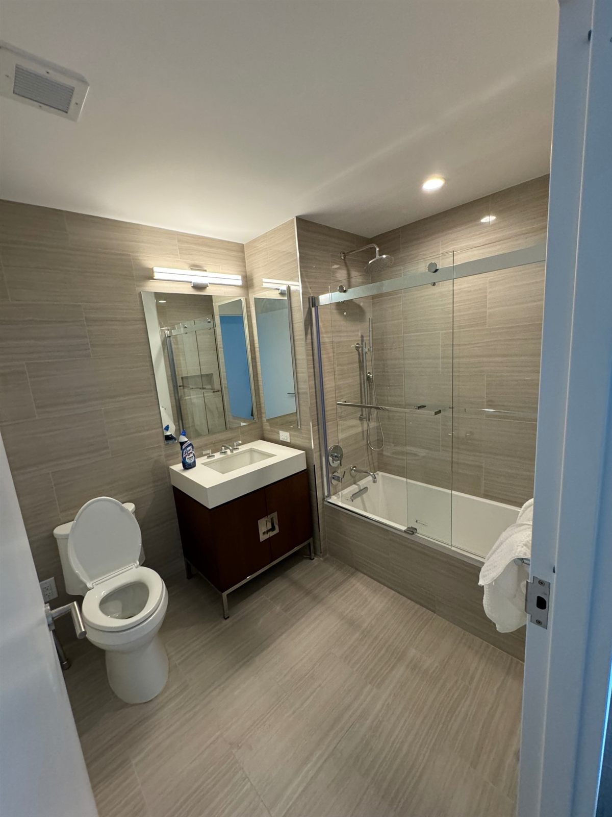 Bathroom with linear-grain porcelain tile, soaking tub with frameless sliding glass doors, and walnut vanity