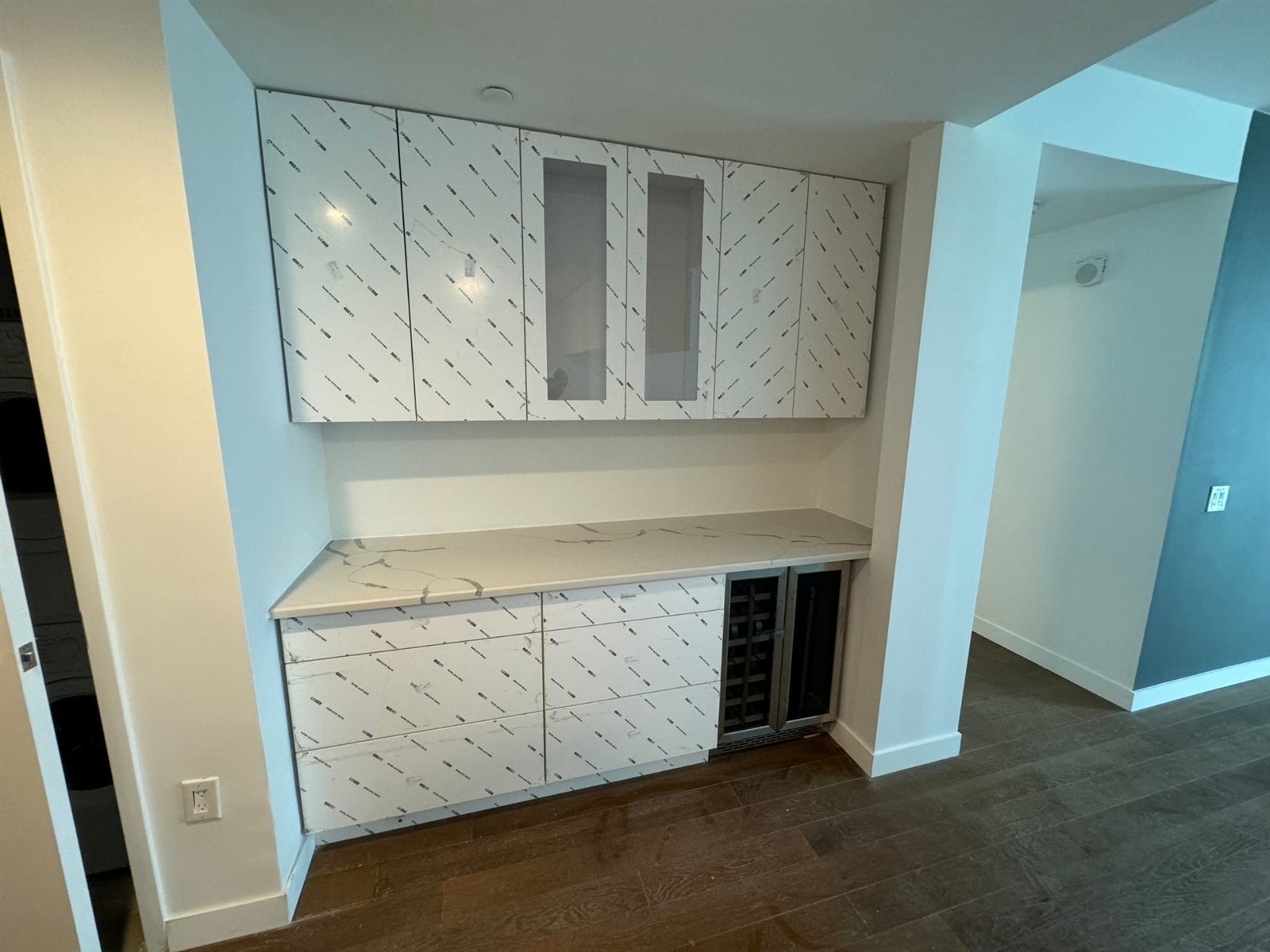Built-in bar with flat-panel cabinets, glass-front uppers, marble-look quartz top, and wine fridge