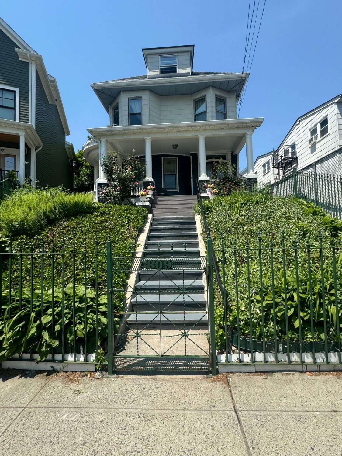 Front porch with white columns, refinished front stairs, and green iron fence and gate