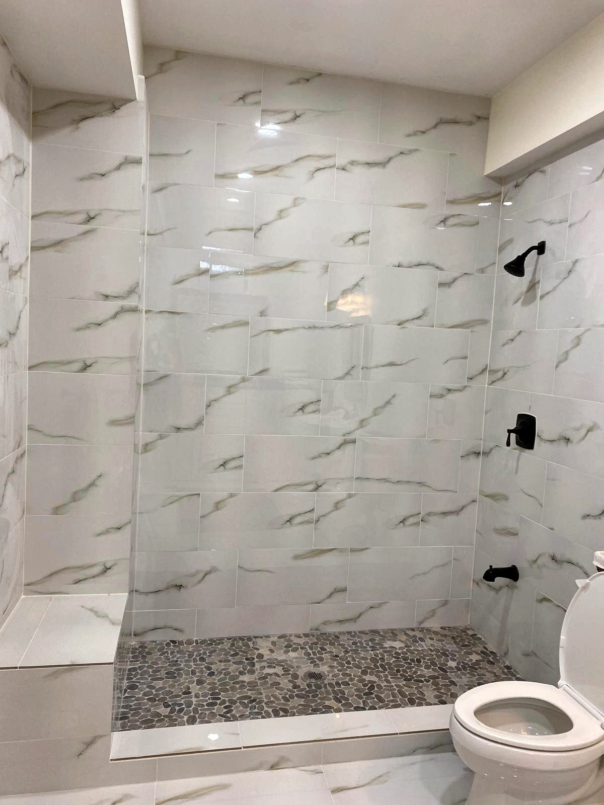 Marble-look tile shower with pebble floor and bench